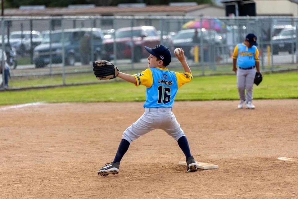 Young pitcher in a light blue jersey delivering from the mound
